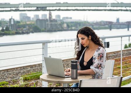 Femme travaillant sur un ordinateur portable à une petite table à l'extérieur sur le toit Banque D'Images