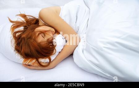 Vue de dessus de belle, jeune, rouge-cheveux femme embrassant dans le lit un oreiller blanc doux, est de profiter de la literie douce fraîche dans la chambre avec l'espace libre pour votre Banque D'Images