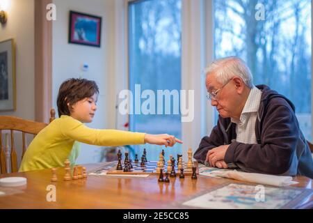 Un garçon fait un mouvement d'échecs tandis que son grand-père regarde activé Banque D'Images