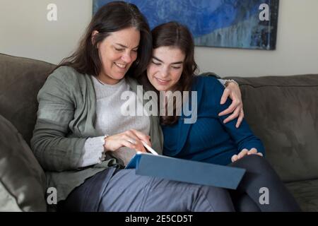 Mère avec le bras autour de l'adolescence fille souriant et regardant tablette Banque D'Images