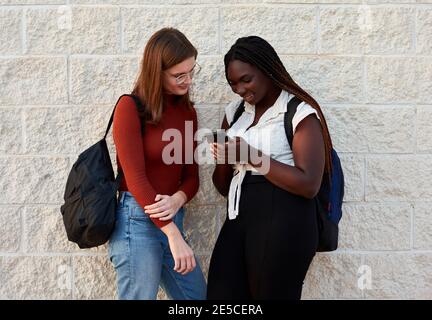 Deux jeunes femmes regardent leur smartphone. Concept multiethnique Banque D'Images