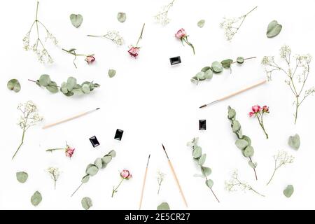 Espace de travail avec pinceaux et boutons roses, feuilles d'eucalyptus sur fond blanc. Cadre d'art pose à plat, vue du dessus, espace de travail pour bureau à domicile Banque D'Images