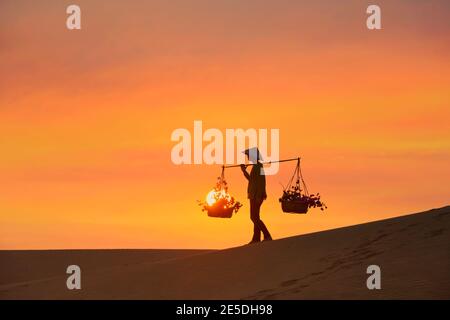 Femme portant des paniers sur une dune de sable au coucher du soleil, Mui ne, Vietnam Banque D'Images