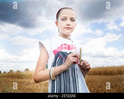 Belle fille debout dans un champ tenant une oreille de blé, Pologne Banque D'Images