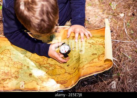 Garçon assis sur le sol de la forêt à l'aide d'une boussole sur une vieille carte. Banque D'Images