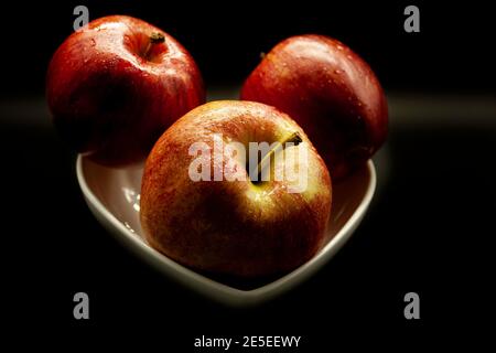 Trois pommes fraîches disposées dans un bol blanc sur un fond noir prêt à manger Banque D'Images