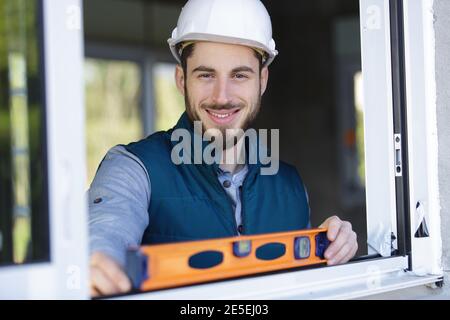 workman utilisant le niveau à bulle pour vérifier l'installation de la fenêtre Banque D'Images