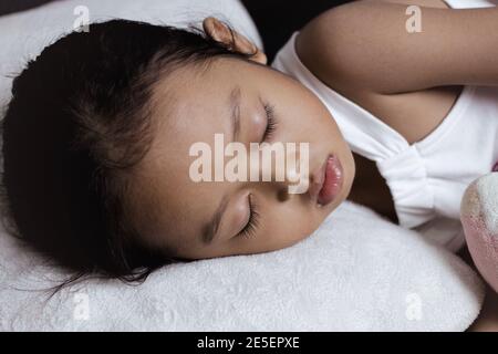 Adorable petite fille dormant avec un jouet préféré sur un canapé noir. Banque D'Images