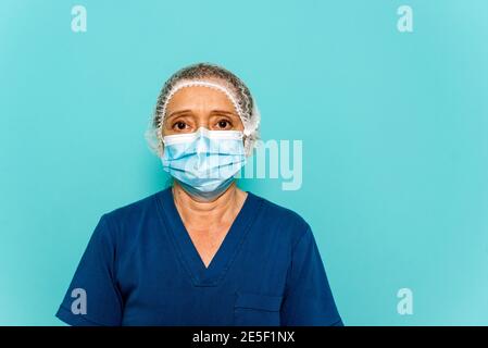 Photo de stock de professionnel de la santé portant un masque facial et un filet de cheveux jetable regardant l'appareil photo contre fond bleu. Banque D'Images