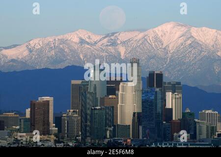 Une pleine lune s'élève au-dessus de la ligne d'horizon du centre-ville de Los Angeles avec les montagnes enneigées de San Gabriel comme toile de fond le mercredi 27 janvier 2021. Banque D'Images