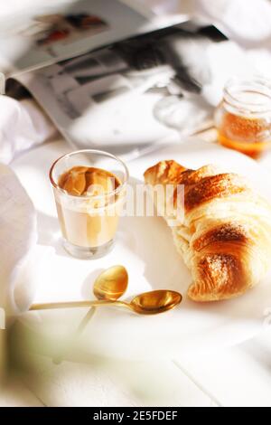 Petit déjeuner en gros avec croissant, latte, sirop de miel et un magazine. Banque D'Images