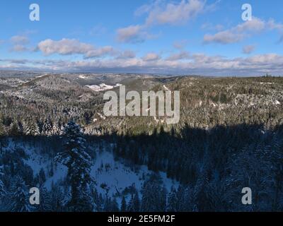 Vue panoramique sur les collines et les vallées de la Forêt-Noire en partie à l'ombre avec forêt et arbres enneigés en hiver. Banque D'Images