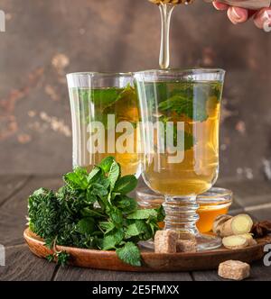 Infusion de fines herbes chaudes dans des verres pour les jours froids. Deux tasses de thé au gingembre avec menthe, thym et miel sur une table en bois. Mise au point sélective. Banque D'Images