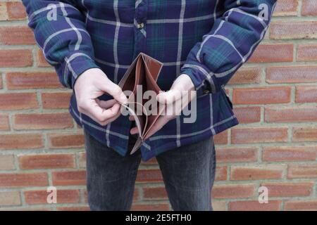 Homme sans argent montrant vide portefeuille avec mur de brique derrière Banque D'Images