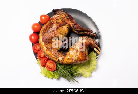 Viande de lapin cuite avec des légumes et des herbes sur une assiette sur fond blanc. Avec tomates et laitue, vue du dessus. Banque D'Images