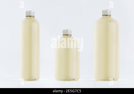 Assortiment de trois bouteilles hautes, basses et épaisses en plastique avec boisson fraîche pâle ou huile essentielle cosmétique, maquette de bouchon argenté sur fond blanc, templa Banque D'Images