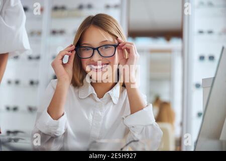 Jolie fille adolescente en chemise blanche regardant et posant à la caméra en clinique d'ophtalmologie Banque D'Images