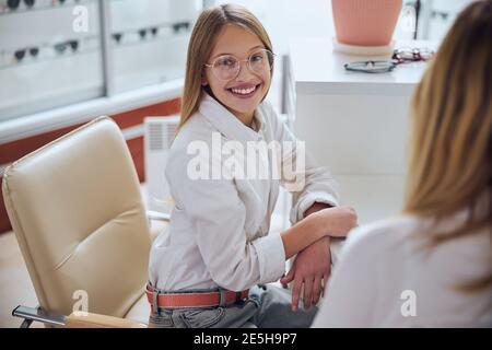 Belle adolescente élégante en lunettes posant à la photo caméra en centre d'ophtalmologie Banque D'Images