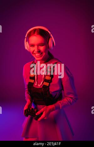 KIEV, UKRAINE - 27 NOVEMBRE 2020 : une femme joyeuse dans un casque sans fil tenant le joystick sur le violet Banque D'Images