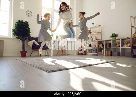 Une jeune femme heureuse et ses enfants sautant et riant salon confortable avec lumière du soleil Banque D'Images