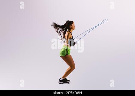 Jeune femme fit corde à sauter. Portrait of muscular young woman jumping rope sur fond blanc gris. Banque D'Images