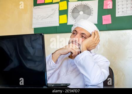 le jeune arabe pense dans son travail avec un regard sérieux sur son visage devant cet ordinateur portable Banque D'Images