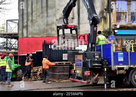 Chantier de construction avec des blocs de béton livrés par le véhicule avec une grue à l'arrière arrêtée sur la route, les ouvriers dirigent le placement des palettes. Très const Banque D'Images