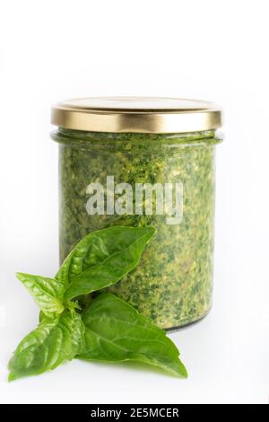 Sauce pesto dans un pot en verre isolé avec des feuilles de basilic frais sur fond blanc. Sauce traditionnelle italienne maison pesto et feuilles de basilic Banque D'Images