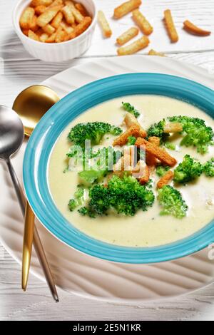 soupe à la crème avec brocoli et croûtons dans un bol bleu sur une table blanche en bois avec des cuillères, vue verticale d'en haut, gros plan Banque D'Images