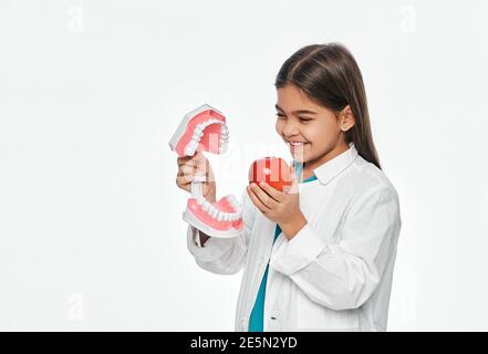 Enfant Latino avec un sourire goûtant, tenant un modèle de mâchoire et de pomme dans ses mains. Les fruits sont très sains pour les dents des enfants Banque D'Images