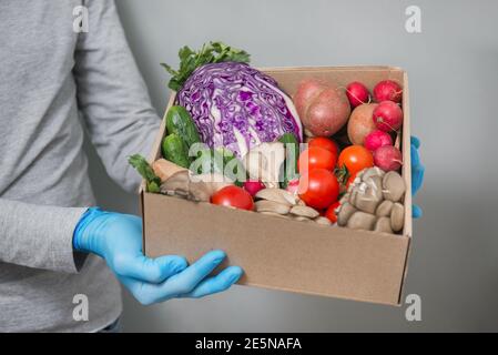 Livraison de légumes frais dans une boîte en papier avec des gants sûrs pendant la quarantaine du coronavirus Banque D'Images