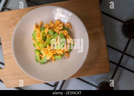 Dans un plat rond, mélanger la gourde amère frite avec l'œuf. Plat poser un plat de nourriture saine sur la planche à découper en bois qui a mis sur la cuisinière comme arrière-plan. Vue de dessus cuisine ima Banque D'Images