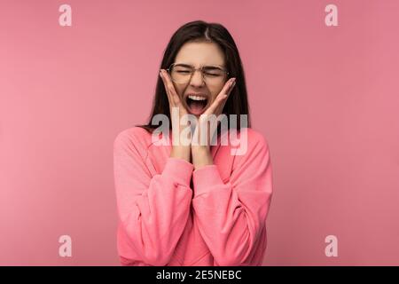 Photo d'une jeune femme attrayante en lunettes criant. Porte un t-shirt décontracté rose isolé de couleur rose fond Banque D'Images