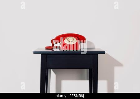 un téléphone fixe rotatif rouge sur une table en bois noir, à l'intérieur, devant un mur blanc Banque D'Images