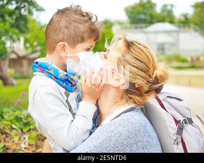 La mère avec son fils dans le masque facial voyagent. Ils embrassent et embrassent. La mère et l'enfant portent un masque facial lors d'une éclosion de coronavirus ou de grippe. Banque D'Images