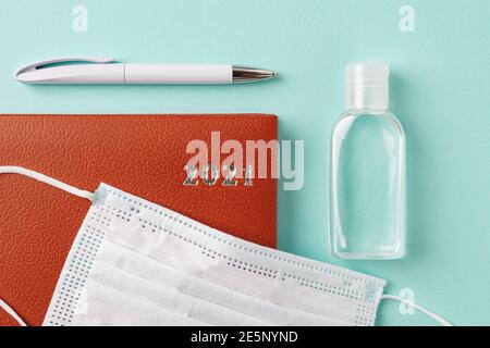 agenda en cuir rouge de 2021 ans, stylo, désinfectant pour les mains et masque médical sur fond turquoise. Planification de la vie et des affaires compte tenu de l'épidémie Banque D'Images