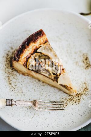 Morceau de cheesecake à la poire sans sucre végétalien sans lait dans une assiette rustique et poire fraîche sur fond de table en marbre blanc, mise au point sélective, gros plan. Concept végétarien moderne de dessert sain Banque D'Images