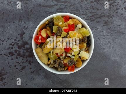 Vue de dessus d'un bol blanc rempli de plusieurs variétés de fruits secs sur une table marbrée. Banque D'Images