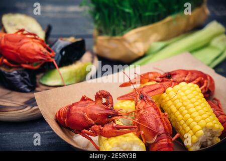 Écrevisse bouillie rouge servant avec des légumes grillés et de la verdure sur une table en bois sombre, vue du dessus Banque D'Images