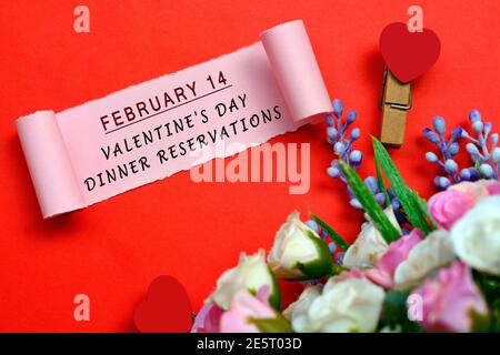 Février 14 Saint-Valentin dîner réservations étiquette sur papier déchiré avec fleurs et coeur en forme de corde à linge sur fond rouge. Concept de la Saint-Valentin Banque D'Images