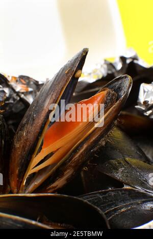 Livraison de nourriture dans un emballage en plastique à votre maison. Moules dans une sauce en papier d'aluminium et contenant en plastique sur fond jaune. Banque D'Images