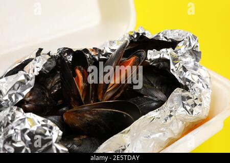 Livraison de nourriture dans un emballage en plastique à votre maison. Moules dans une sauce en papier d'aluminium et contenant en plastique sur fond jaune. Banque D'Images