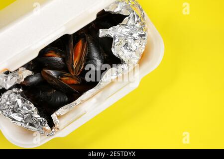 Livraison de nourriture dans un emballage en plastique à votre maison. Moules dans une sauce en papier d'aluminium et contenant en plastique sur fond jaune. Banque D'Images