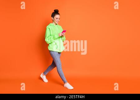 Portrait de la femme en plein écran avec un message texte tenant le téléphone deux mains marchant isolées sur un fond orange vif Banque D'Images