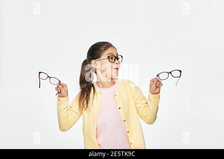 Quel genre de lunettes choisir de l'enfant. Drôle asiatique fille portant des lunettes tenant des lunettes stylées sur fond blanc Banque D'Images