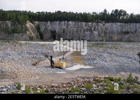 Vue à l'intérieur d'une carrière de granit avec machine jaune lourde. Matériel minier, paysage industriel. Banque D'Images