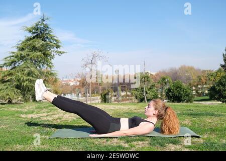 REDHEAD femme caucasienne s'exerçant dans un parc avec un tapis. Fitness et sport en plein air. Banque D'Images