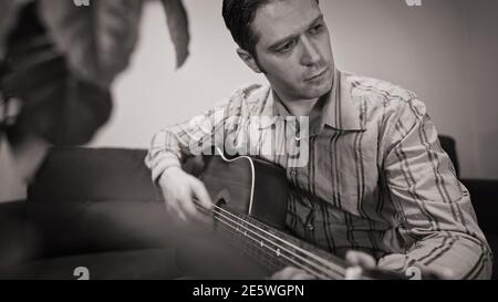 Beau homme jouant de la guitare en nylon à la maison. Noir et blanc. Banque D'Images