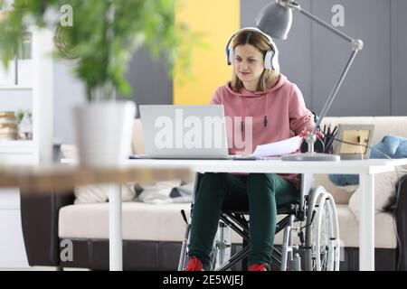 Jeune femme en fauteuil roulant travaillant sur un ordinateur portable à la maison Banque D'Images