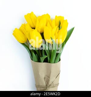 Bouquet de tulipes jaunes enveloppées de papier artisanal sur fond blanc. Banque D'Images